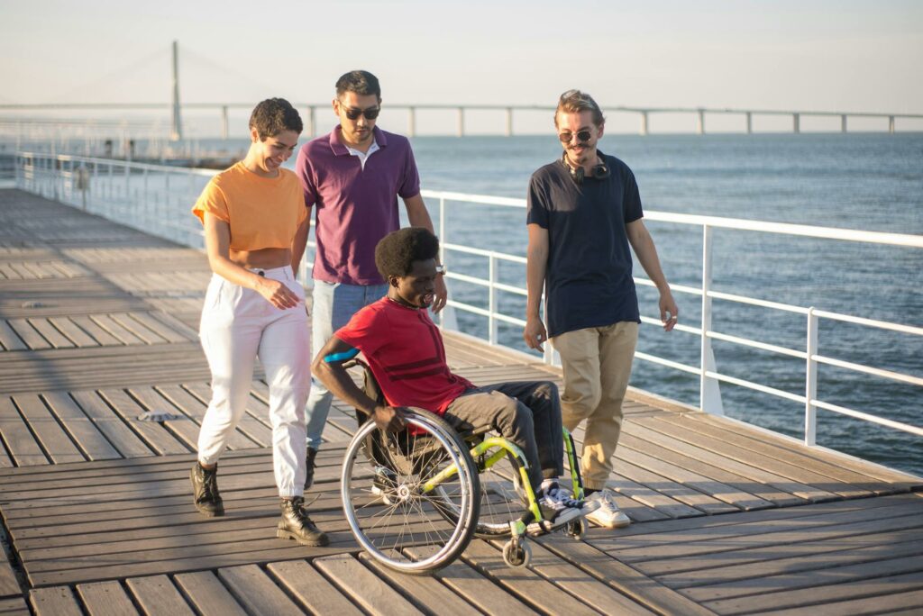 A group of friends of various races and abilities talk a walk/roll alongside a pier. Several of them are enrolled in IHS.