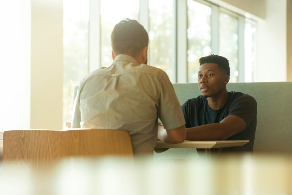 A young man receiving services sits across a table from a consultant. They discuss how to write the CFSS Service Delivery Plan.