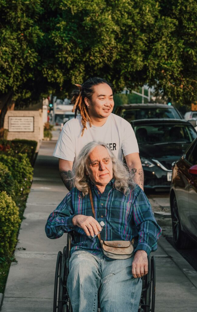 A HMC residential services volunteer pushes an elderly man in a wheelchair.